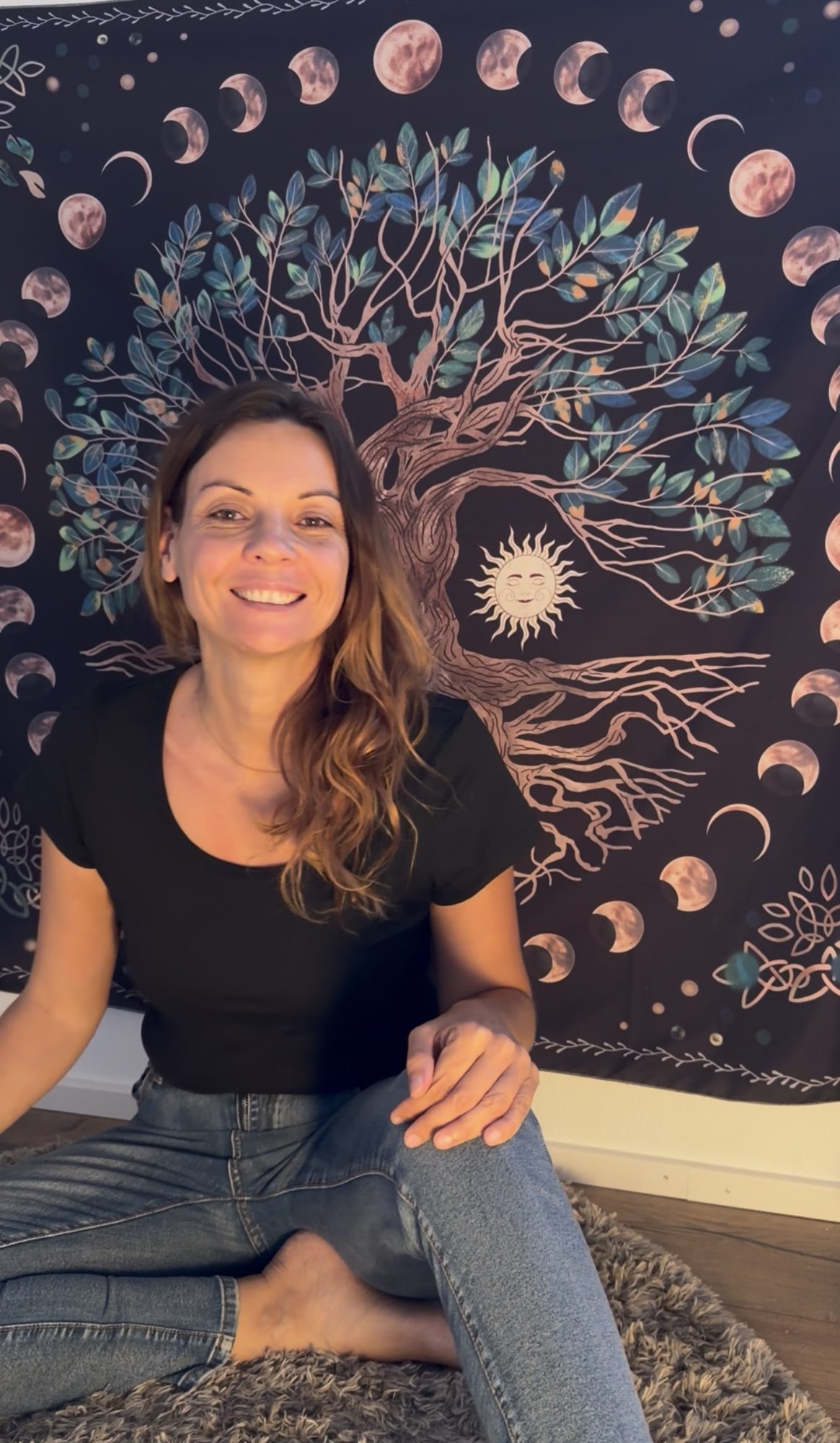 Melanie Gruber sitzt am Boden vor einem Lebensbaum mit Sonne und Mond